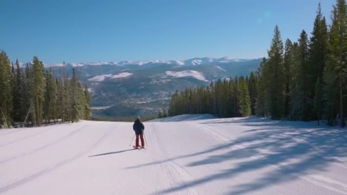 在冬季森林景观中，与远处的山脉一起，在修饰的空滑雪坡上追踪一名滑雪者