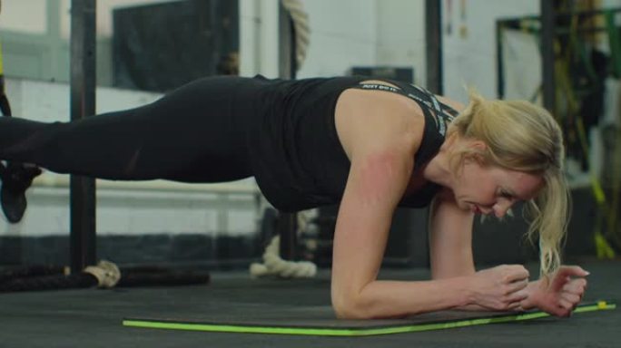 健身女子在健身房的垫子上做木板运动锻炼。女运动员在健身房的地板上做铺板运动。