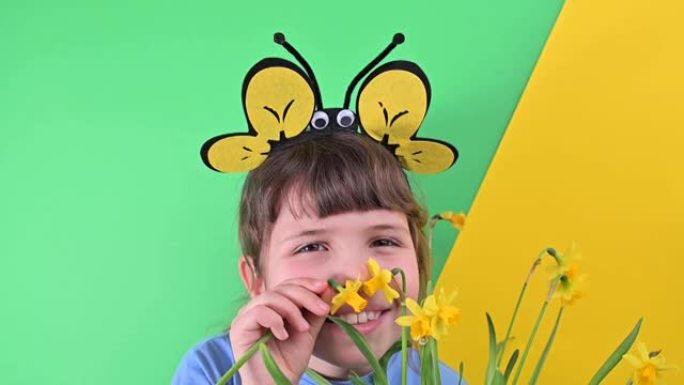 一个小女孩躲在绿色背景下的黄色水仙花后面。戴蜂帽的快乐孩子拿着一盆花园花。春天在花园里种植季节。选择