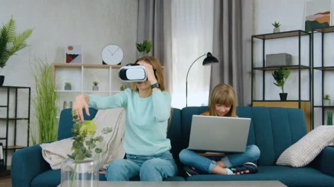 美丽积极的现代两个不同年龄的女孩共同休闲玩虚拟游戏使用笔记本电脑和增强现实护目镜，前视图