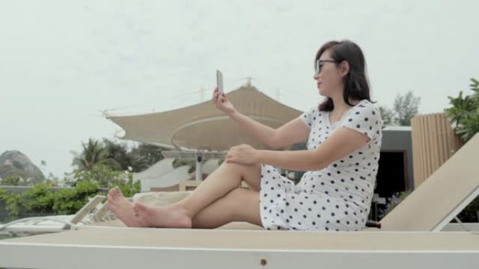 快乐的亚洲人在度假期间在酒店的日光浴床上拍照或自拍，放松，生活方式理念。