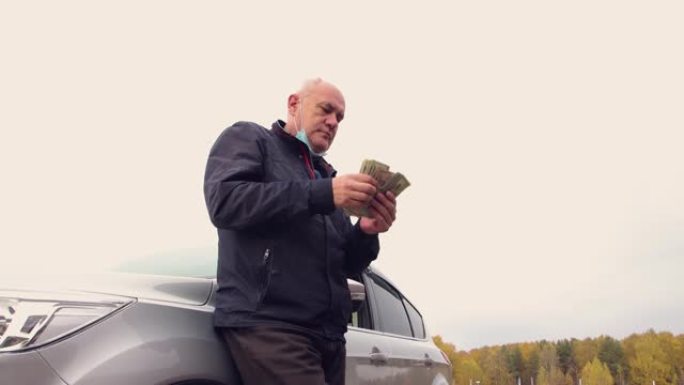 站在汽车旁边的一个快乐的人算美元-他的收入。