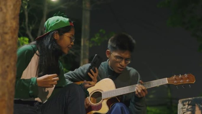 年轻的亚洲男女在智能手机设备上唱歌和弹吉他。
