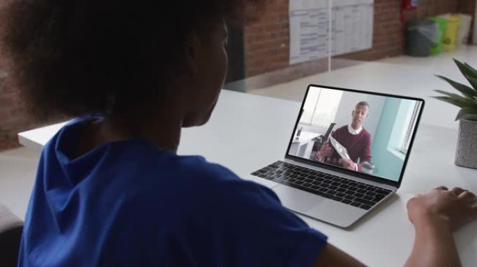 非裔美国妇女在办公室的笔记本电脑上与男同事进行视频通话的后视图