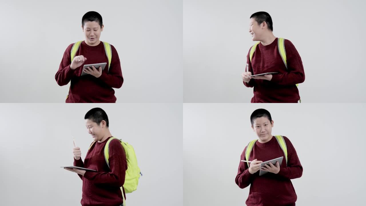 穿着红色毛衣的亚洲男生在灰色背景下用数字平板电脑写字笔记，教育生活方式理念。