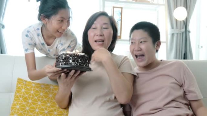 快乐的亚洲儿童在家里，母亲节或生日概念的沙发上一起用巧克力蛋糕给妈妈惊喜。