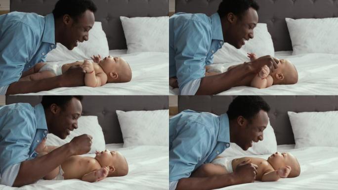 陪产假。快乐的非洲裔美国男子和他可爱的新生婴儿躺在大床上玩耍，微笑着大笑
