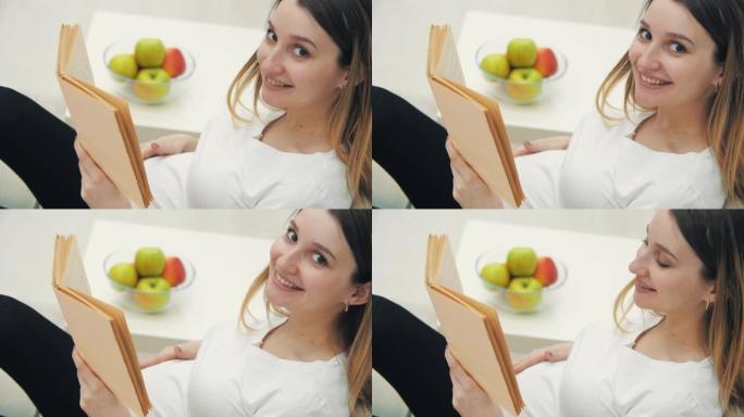 4k的微笑孕妇视频，背景是一本书和一碗水果。