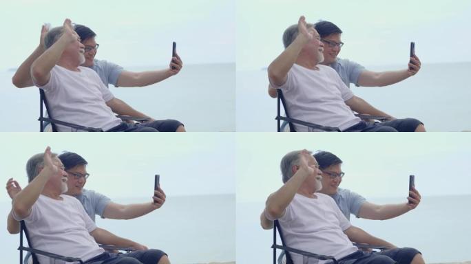 亚洲老人和儿子暑假去海边旅行。年轻人通过视频通话与家人交谈社交媒体概念技术