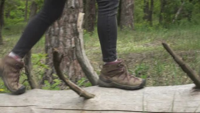 穿着远足靴的徒步旅行者女孩在森林里的树干旁行走的特写镜头