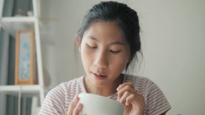 快乐的亚洲女孩在家窗口附近吃冰淇淋，生活方式理念。