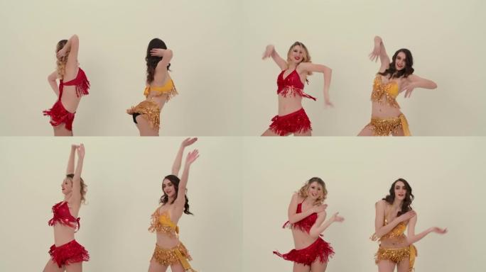 两个穿着红色和黄色闪亮制服的可爱的啦啦队长跳着欢快的舞蹈，移动臀部。啦啦队长在慢动作的白色演播室背景