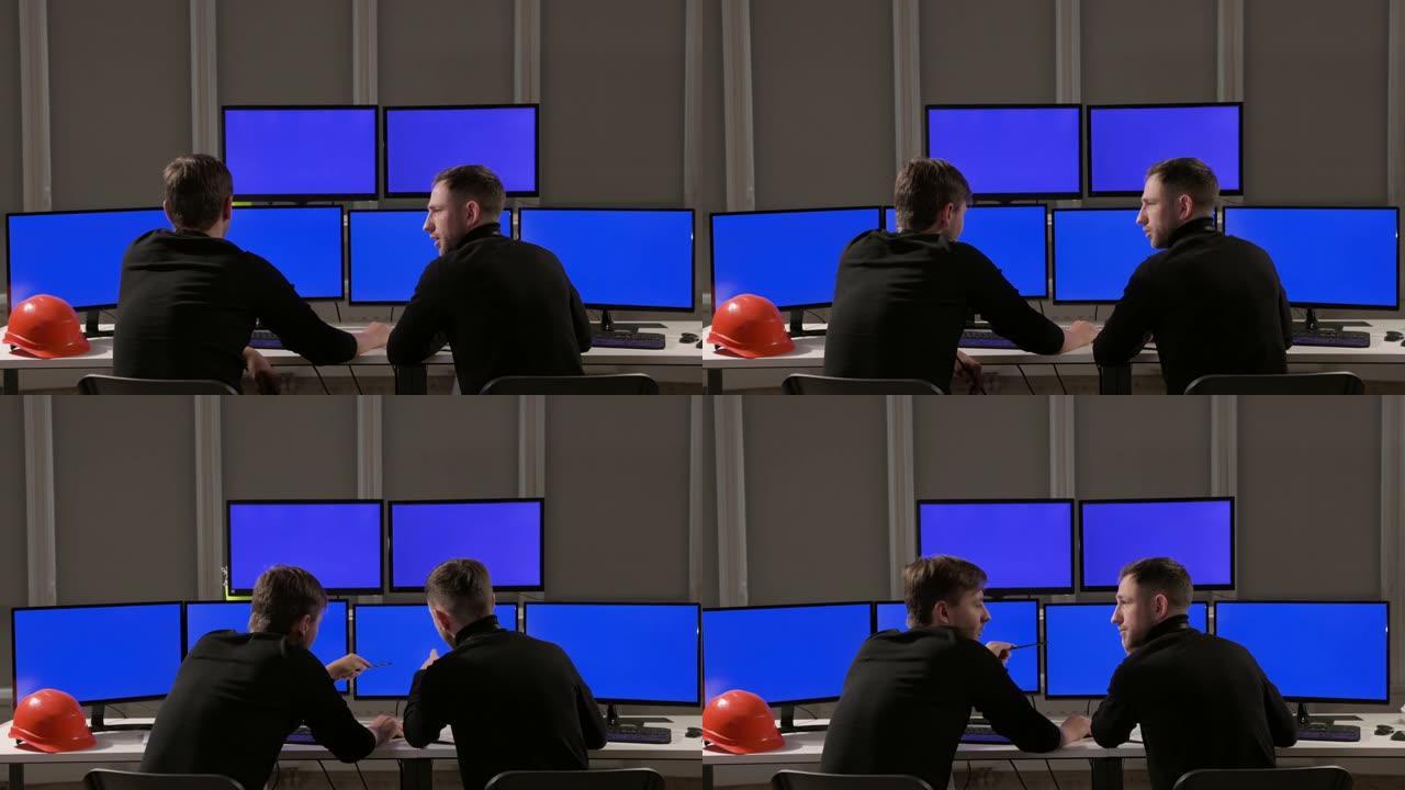 保安人员在电脑屏幕上观看。他们讨论工作流程。其中一个男人喝咖啡。六个监视器。