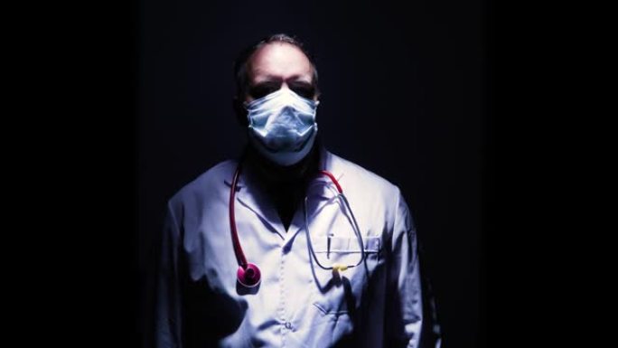 戴着口罩和手套的医生肖像从黑暗中出来，然后凝视着相机鼓掌或为英雄鼓掌，例如与冠状病毒作斗争的护士医生