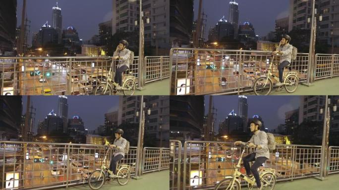 亚洲商人和他的自行车在立交桥路上，并使用具有现代建筑背景的手机