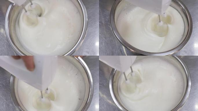 一位男士糕点厨师的特写镜头用搅拌器在碗中鞭打蛋清。