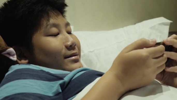 快乐的亚洲男孩在酒店房间的床上玩网络游戏假期与家人，生活方式的概念。