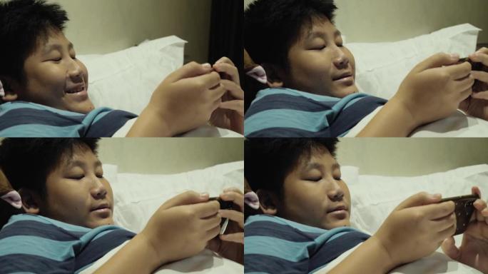 快乐的亚洲男孩在酒店房间的床上玩网络游戏假期与家人，生活方式的概念。