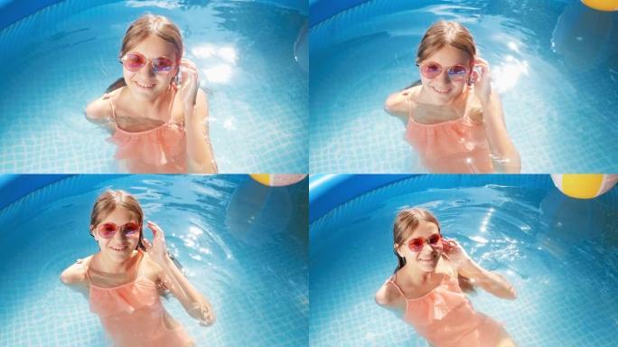 美丽微笑的少女在室外游泳池放松的太阳镜和泳衣的肖像。暑假和假期快乐愉快的概念