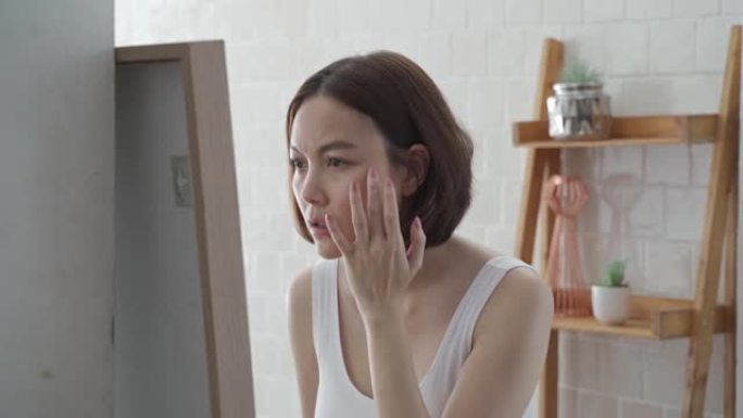 迷人美丽的短发亚洲女性担心照镜子面部护肤状况。沮丧的年轻女性在浴室照镜子时检查自己的脸。恼人的面部年