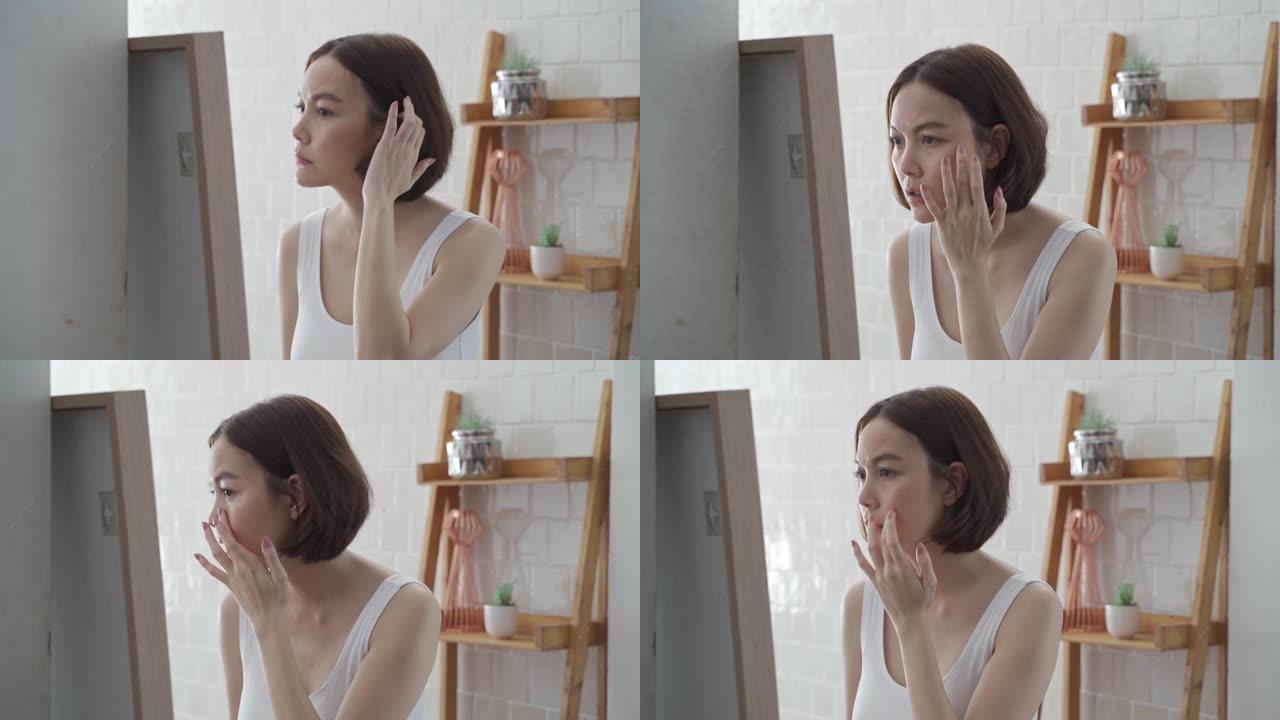 迷人美丽的短发亚洲女性担心照镜子面部护肤状况。沮丧的年轻女性在浴室照镜子时检查自己的脸。恼人的面部年