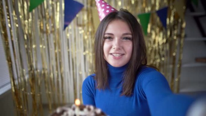 在家聚会一个手里拿着节日蛋糕和蜡烛的女孩在网络摄像头上交流并告诉她的朋友。一个20岁快乐女人的生日。