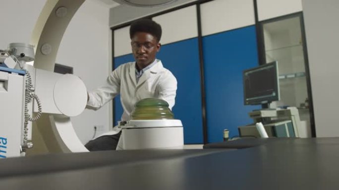 年轻自信的非洲医生穿着白色制服的底视图，与现代碎石机设备一起治疗肾结石。无创体外休克波碎石术
