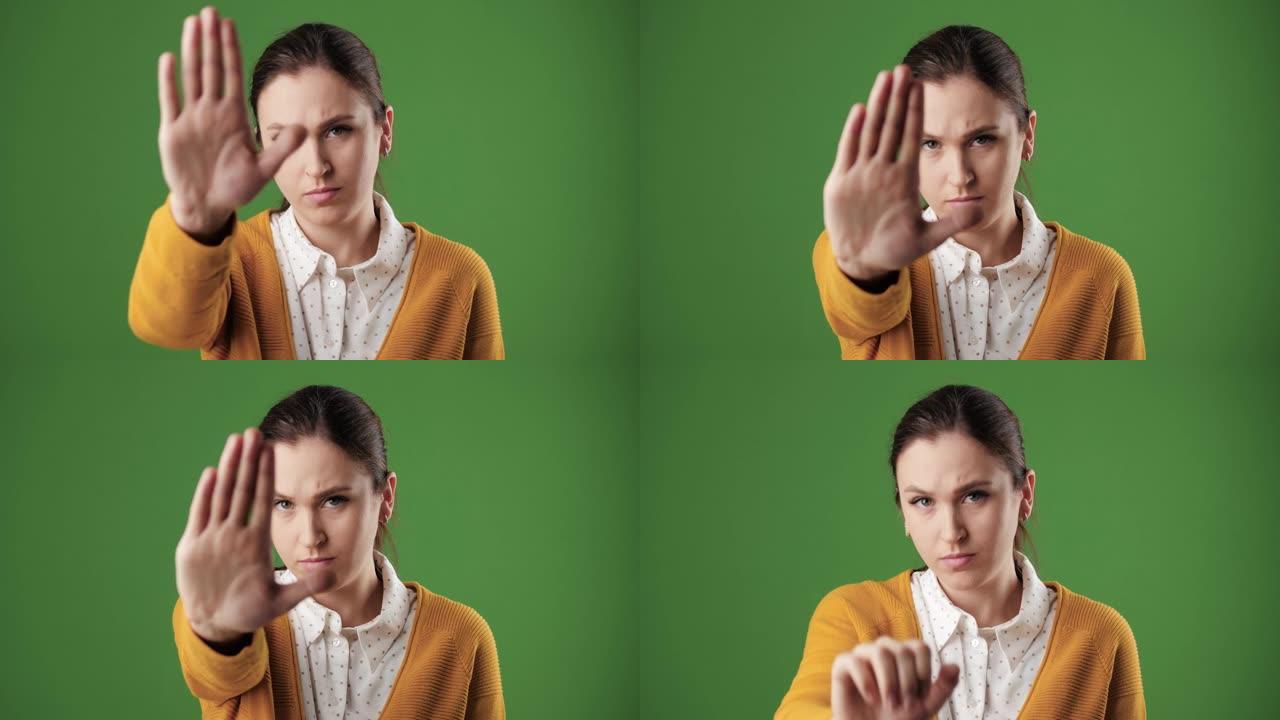女人手掌停止。皱着眉头的严肃的女人在色度关键背景上看着相机举起她的手，显示她的手掌信号停止。慢动作