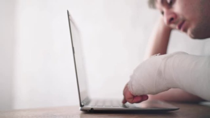 一名手臂受伤的男子看着笔记本电脑。在线诊断。健康保险