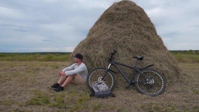 一个骑自行车的人坐在干草堆旁休息。骑自行车的健康人。自由旅行者骑自行车旅行