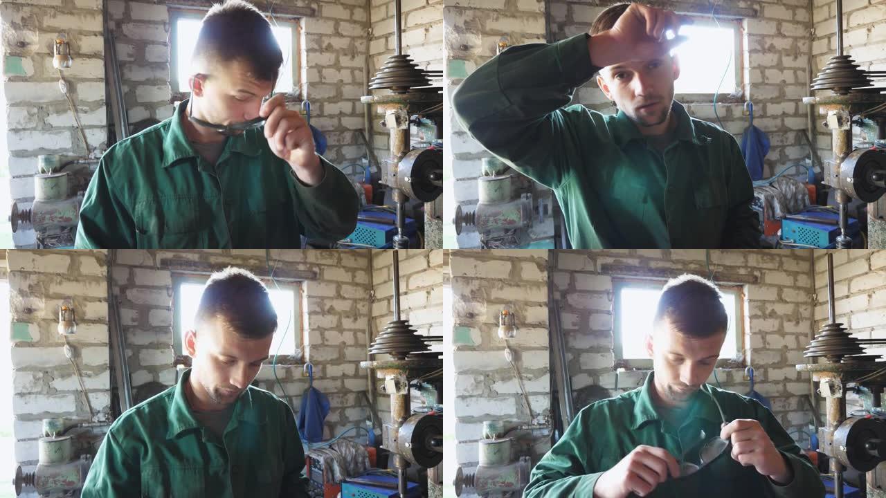 工作服中的男性机械师脱下防护眼镜，擦去额头上的汗水。年轻的修理工戴上眼镜，继续在车库工作。维护服务的