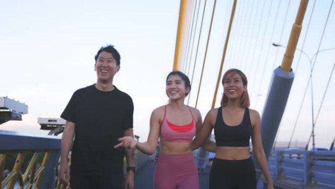 年轻的亚洲男女跑步者在桥上行走的肖像，腰部拥抱，在谈话中放松和大笑，并在日落时从跑步中休息