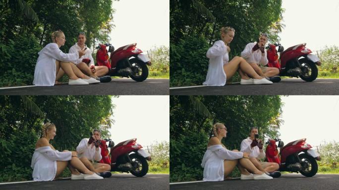 两个白人旅游女人坐在红色滑板车附近。让它自拍。穿着白色衣服骑摩托车的情侣在森林之路小径旅行。