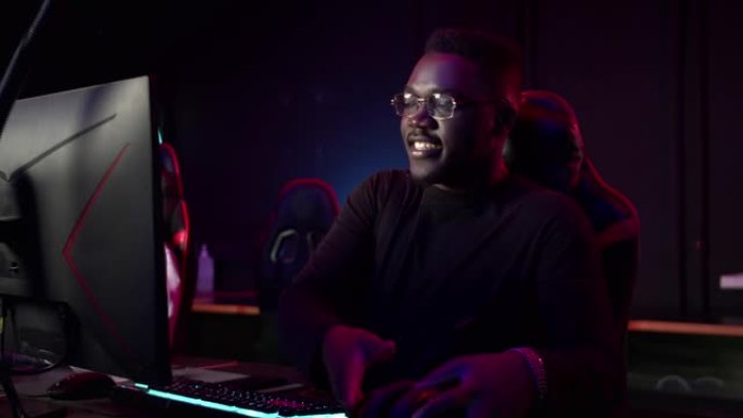 一名非洲学生坐在电脑俱乐部的游戏椅上，戴上耳机，微笑着，为比赛做准备