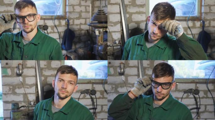穿着制服的精疲力竭的机械师脱下防护眼镜，擦去额头上的汗水。疲惫的年轻修理工戴上眼镜，看着车库里的相机