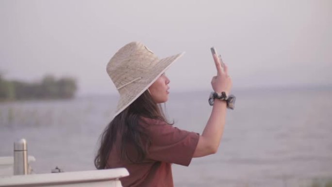 在阳光明媚的日子里，年轻的亚洲女性在湖边的卡车后面用智能手机拍照。