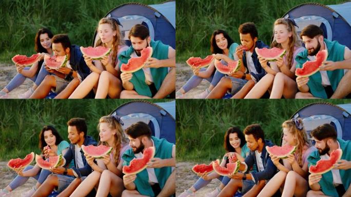 日落时，看起来不错的一群朋友在日落时野餐时在湖边吃美味的西瓜