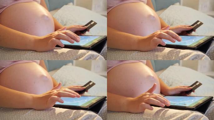 大肚子拿着信用卡和浏览网上商店的孕妇特写镜头。怀孕做网购
