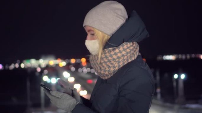 蒙面女孩在夜晚以城市为背景看手机。