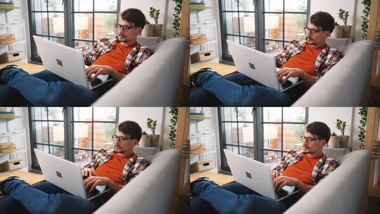 年轻人在沙发上放松，在笔记本电脑上工作