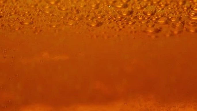 含碳酸液体的啤酒杯细节。大气泡和小气泡以慢动作漂浮在金色啤酒液中。广告用泡沫啤酒的商业背景纹理特写