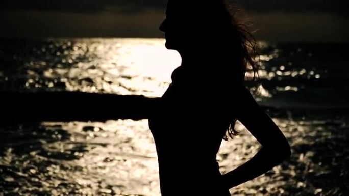 海边一个女人的剪影。用高光和光色对着太阳。头发在风中飞翔