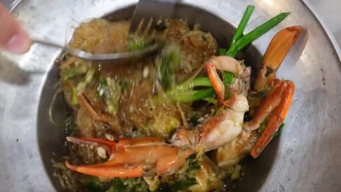 手在锅底将粉丝玻璃面条，蓝蟹鸡蛋和肉与香草菜混合在一起泰国中国菜