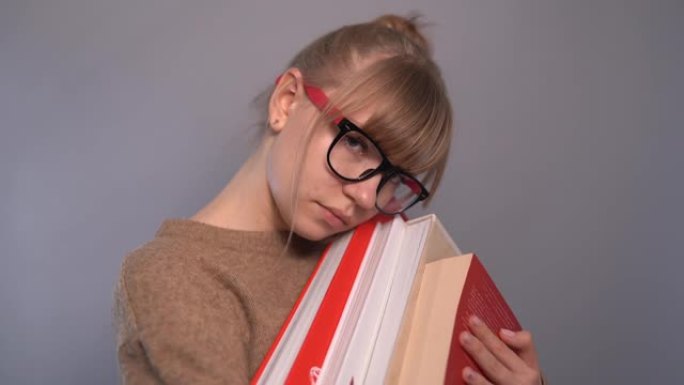 可爱的累了的书呆子学生女孩戴眼镜和一堆书