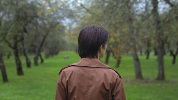 女人在雨中绿树成荫的春天花园中行走的背景图。不露面的女孩在户外享受新鲜空气的空闲时间。时尚时尚孤独孤