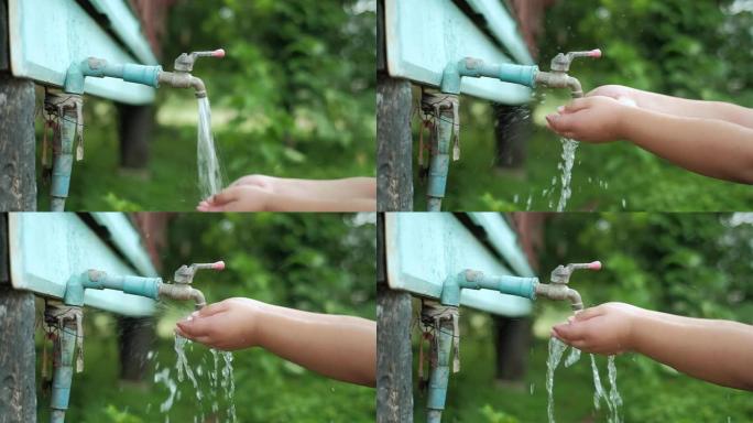 亚洲小男孩的慢动作手在水龙头下打水，纯净水流涌入亚洲小男孩的手。节水理念。