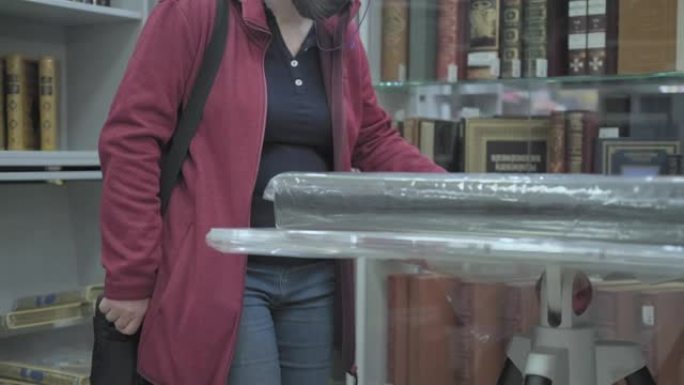 戴眼镜和口罩的白人妇女在商店里检查着巨大的旧书