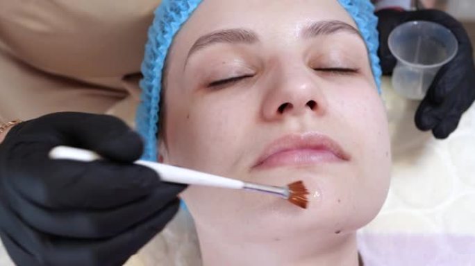 美容师正在美容诊所用刷子在女人的脸上涂抹脱皮面膜。美容师制作护肤程序。美容中的水疗护理