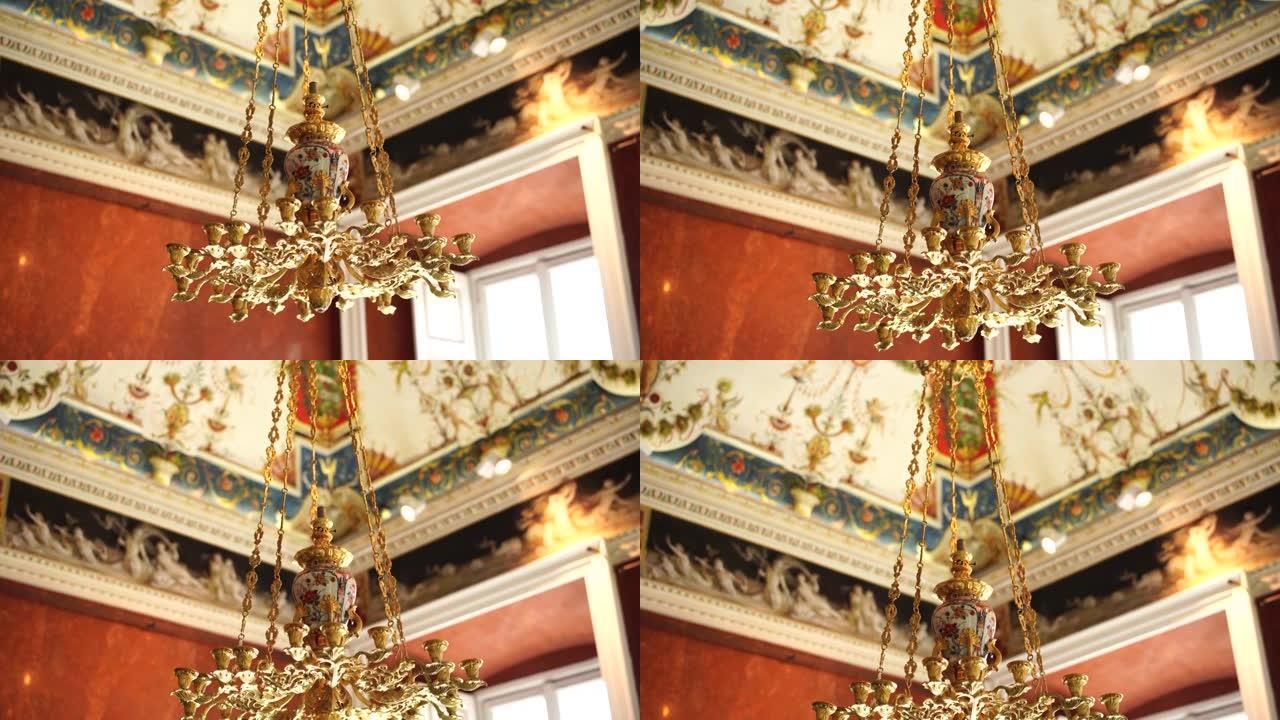 古董金色意大利吊灯的特写镜头。镀金链条上的枝形吊灯挂在彩绘天花板的背景上。