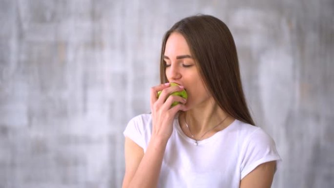 年轻女子咬着吃美味的青苹果。健康的年轻女子吃青苹果，在家微笑-室内